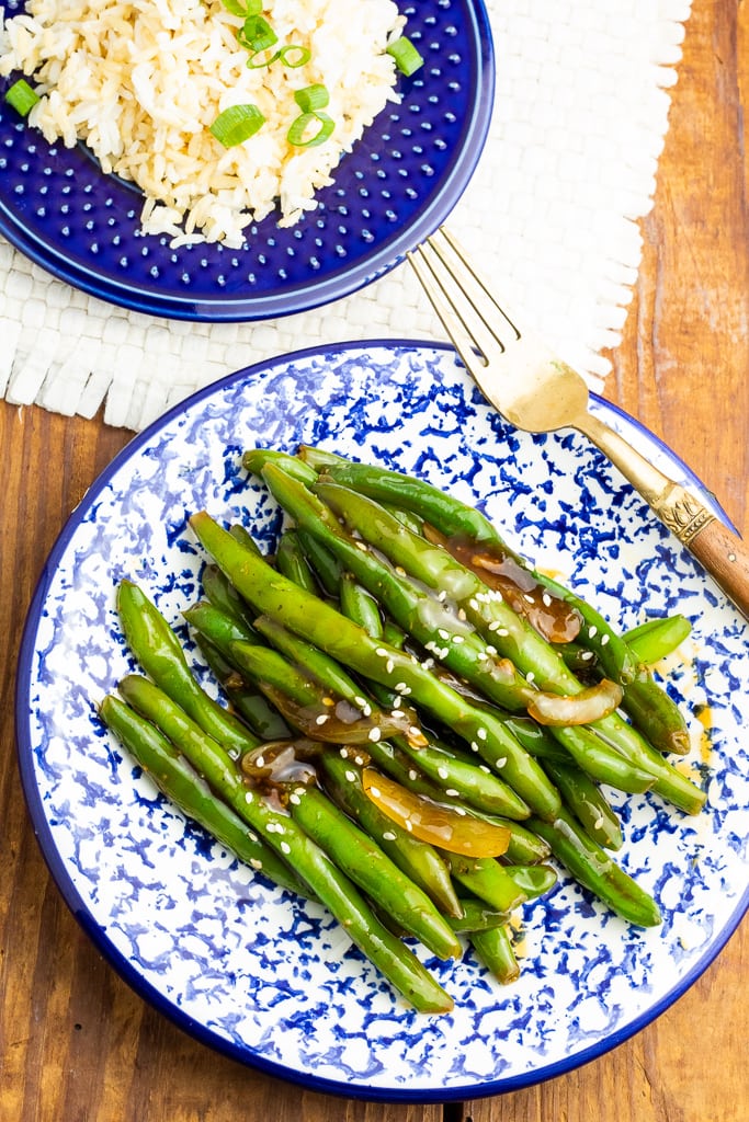 overhead photo of large blue plate with asian green beans and smaller blue plate with rice