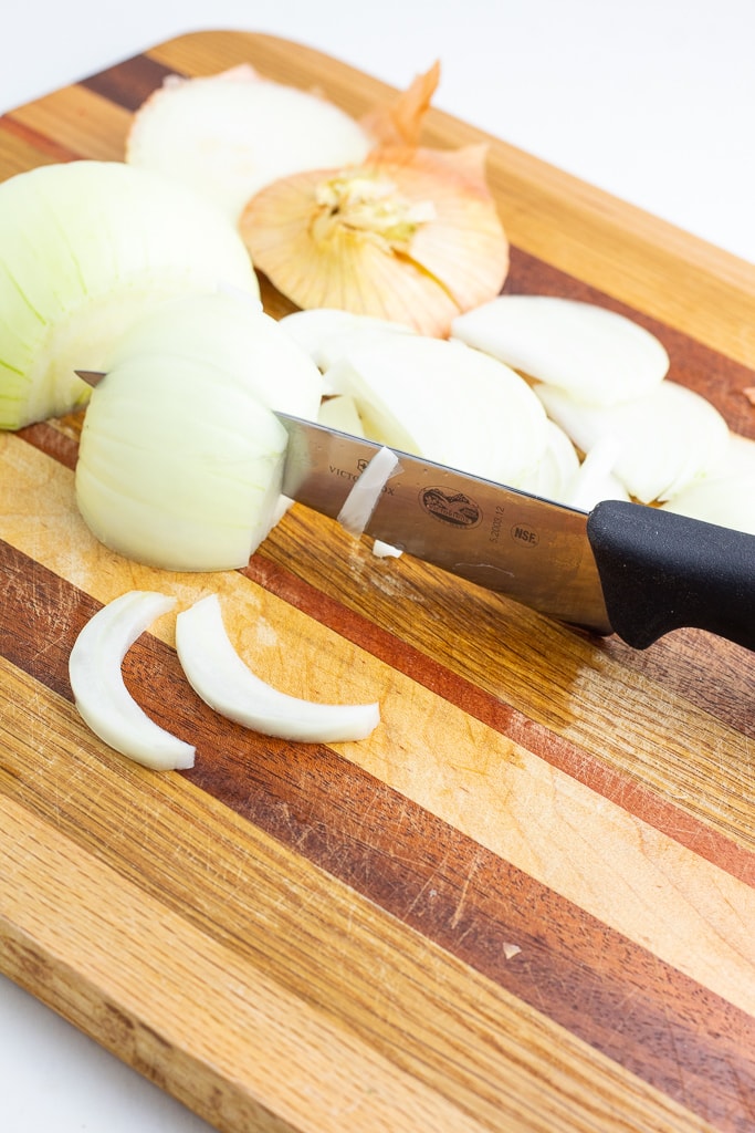 onions being sliced into crescent shapes on wooden cutting board