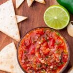 bowl of chunky blender salsa on a wooden cutting board surrounded with homemade tortilla chips and lime.