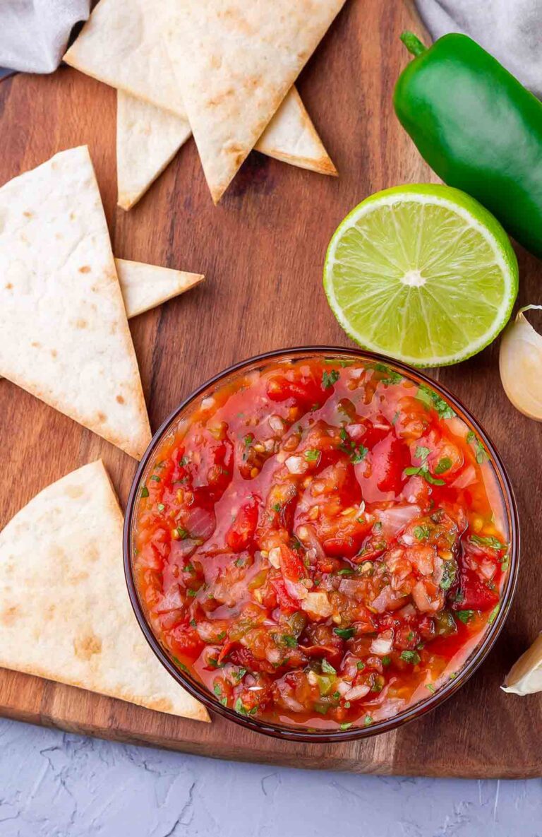 bowl of chunky blender salsa on a wooden cutting board surrounded with homemade tortilla chips and lime.