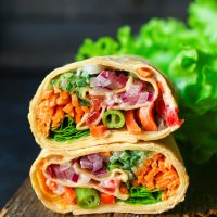 2 veggie wraps stacked on top of each other on a wooden board with lettuce in background