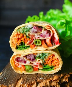 2 veggie wraps stacked on top of each other on a wooden board with lettuce in background