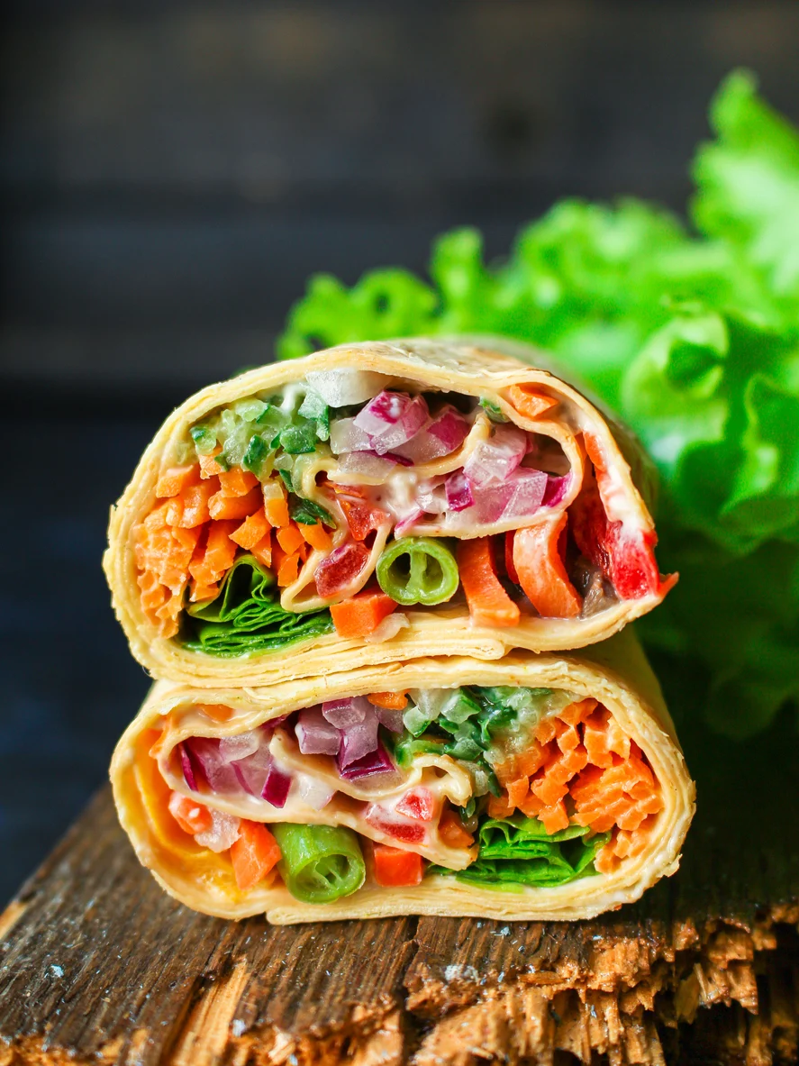 2 veggie wraps stacked on top of each other on a wooden board with lettuce in background.