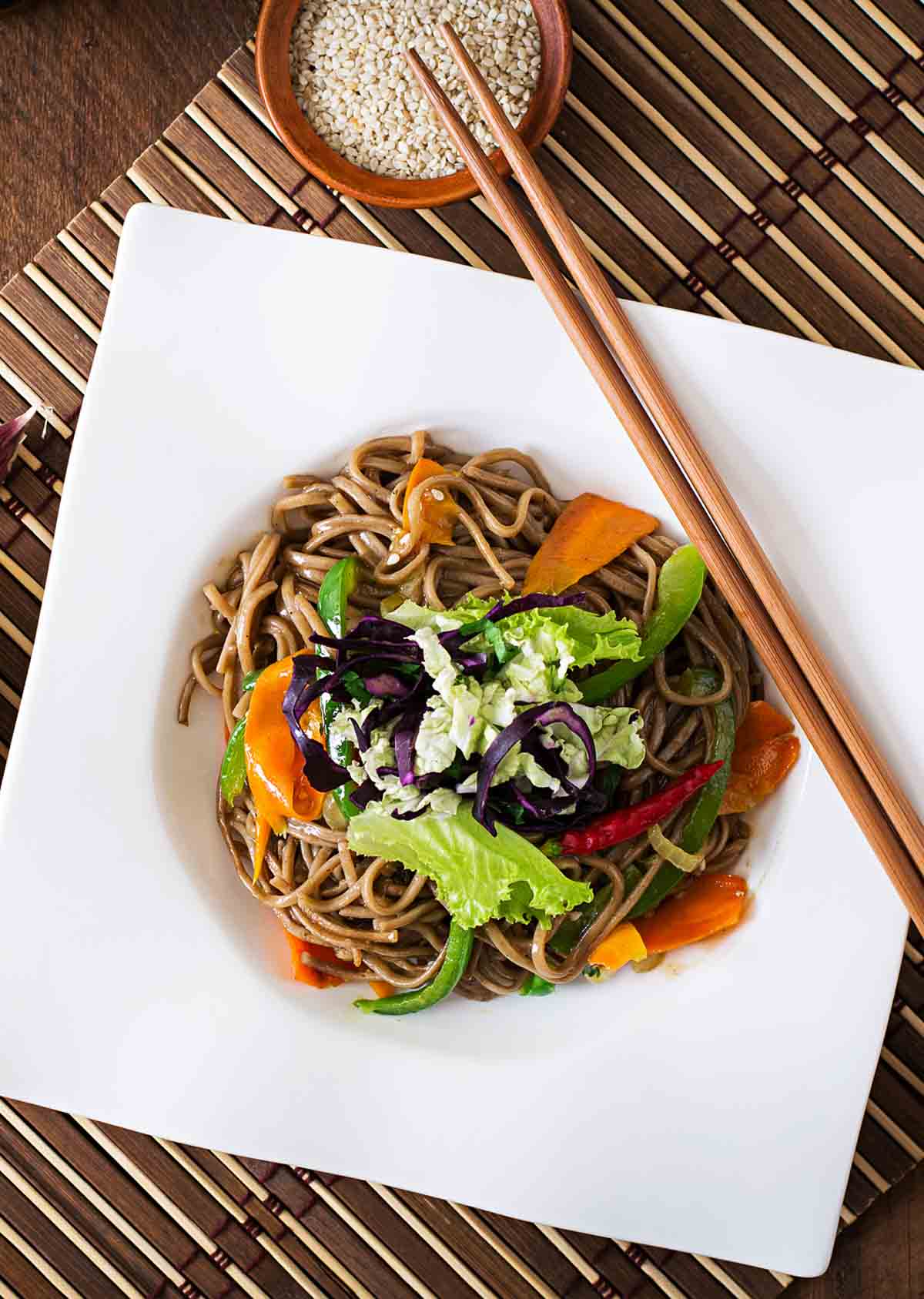 soba noodle veggie stir fry on a white square plate with wooden chopsticks.