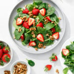 white plate of spinach salad with strawberries and walnuts on white table