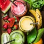 vegetable fruit smoothies in three mason jars with straws surrounded by produce