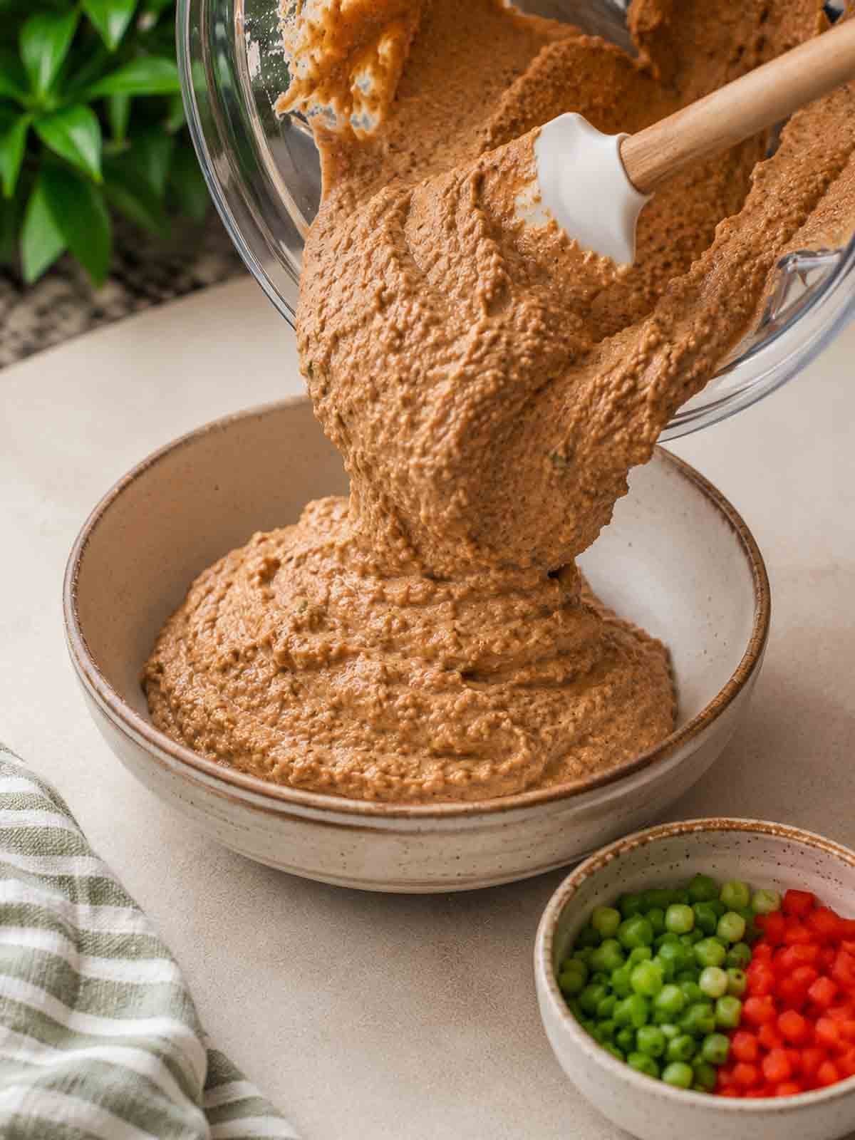 bean dip being poured from blender into a bowl with a spatula.