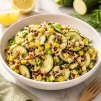 white bowl filled with zuchini corn salad with sliced lemon and zuchinni in background.