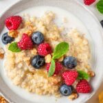 white bowl filled with sweetened quinoa and topped with blueberries and raspberries and plant milk.
