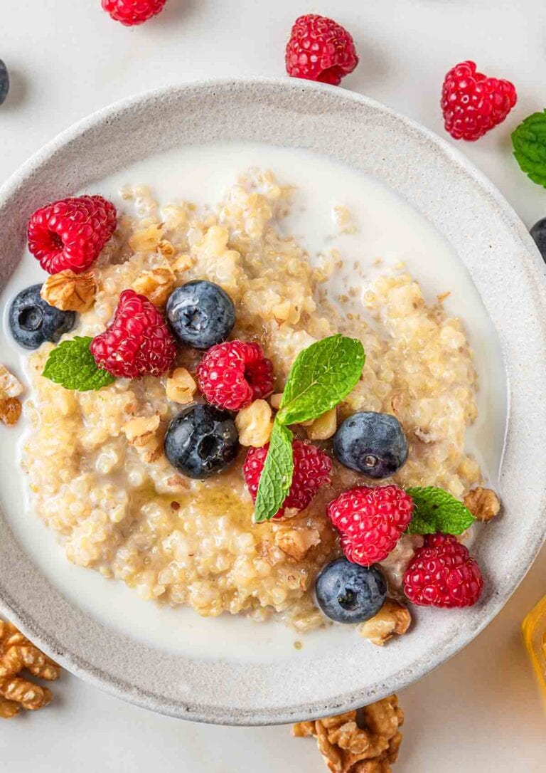 white bowl filled with sweetened quinoa and topped with blueberries and raspberries and plant milk.