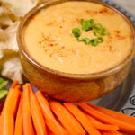 spicy nach dip in brown bowl surrounded by carrot sticks