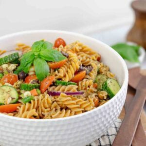 vegetable pasta salad in a white textured bowl topped with basil leaves.
