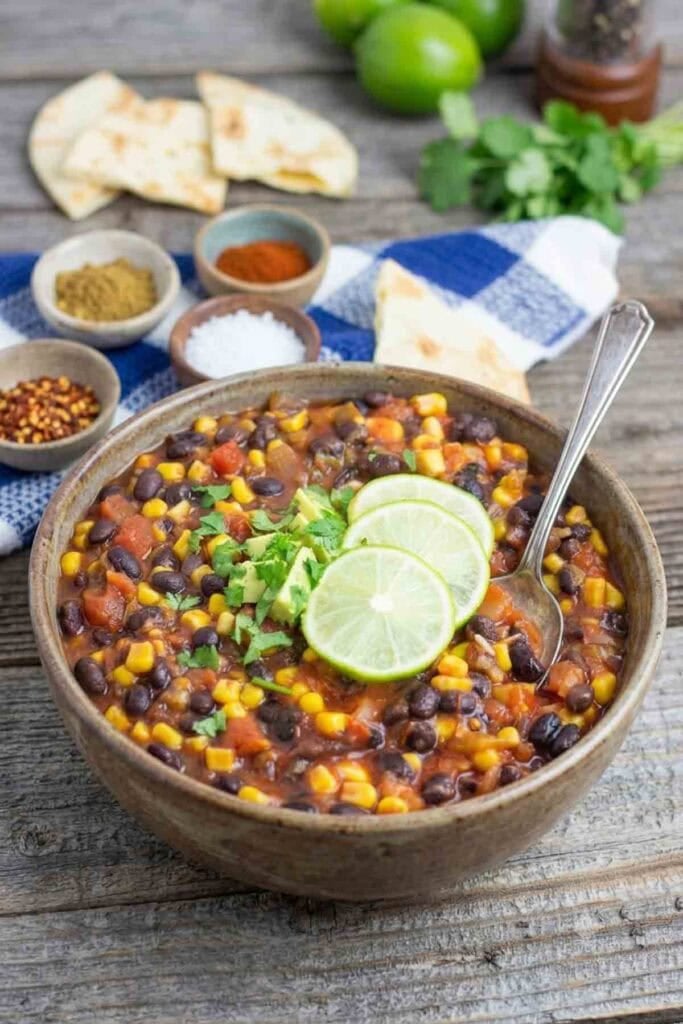 black bean chili in a rustic bowl with a spoon and topped with lime slices.