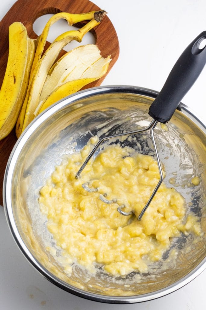 banana being mashed with potato masher in mixing bowl