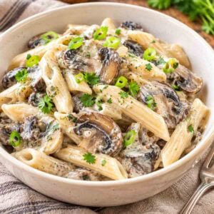 vegan mushroom stroganoff in a white bowl with a few whole mushrooms in the background.