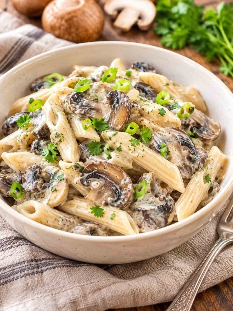vegan mushroom stroganoff in a white bowl with a few whole mushrooms in the background.