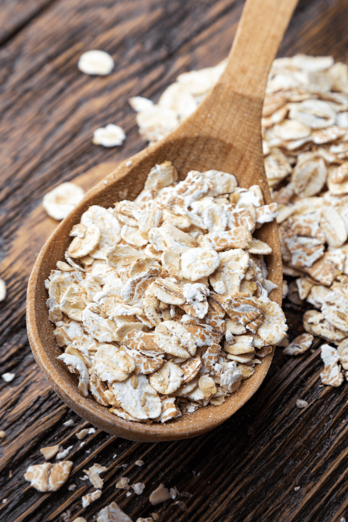 raw oatmeal flakes on wooden spoon and wooden table