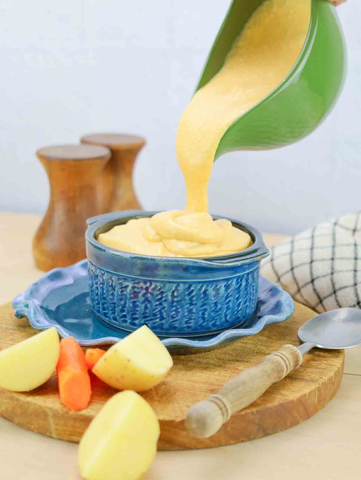 dairy-free cheese sauce being poured into a blue crock dish.