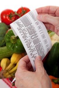 hands holding grocery receipt with vegetable in background