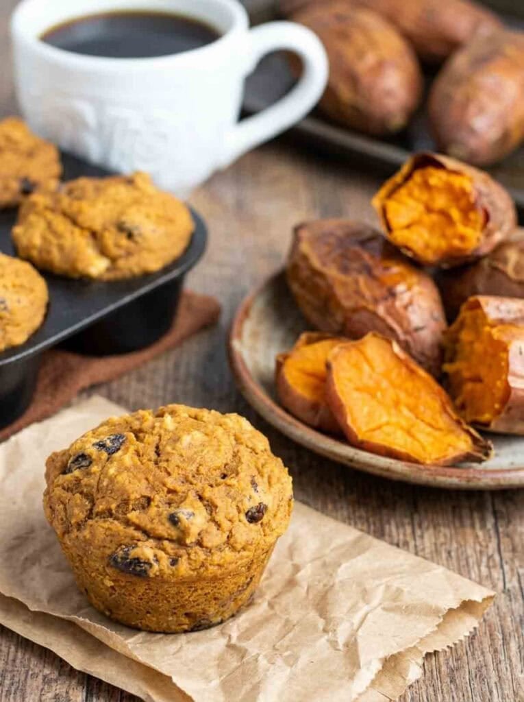 sweet potato muffin on brown parchment paper with baked sweet potatoes in background.