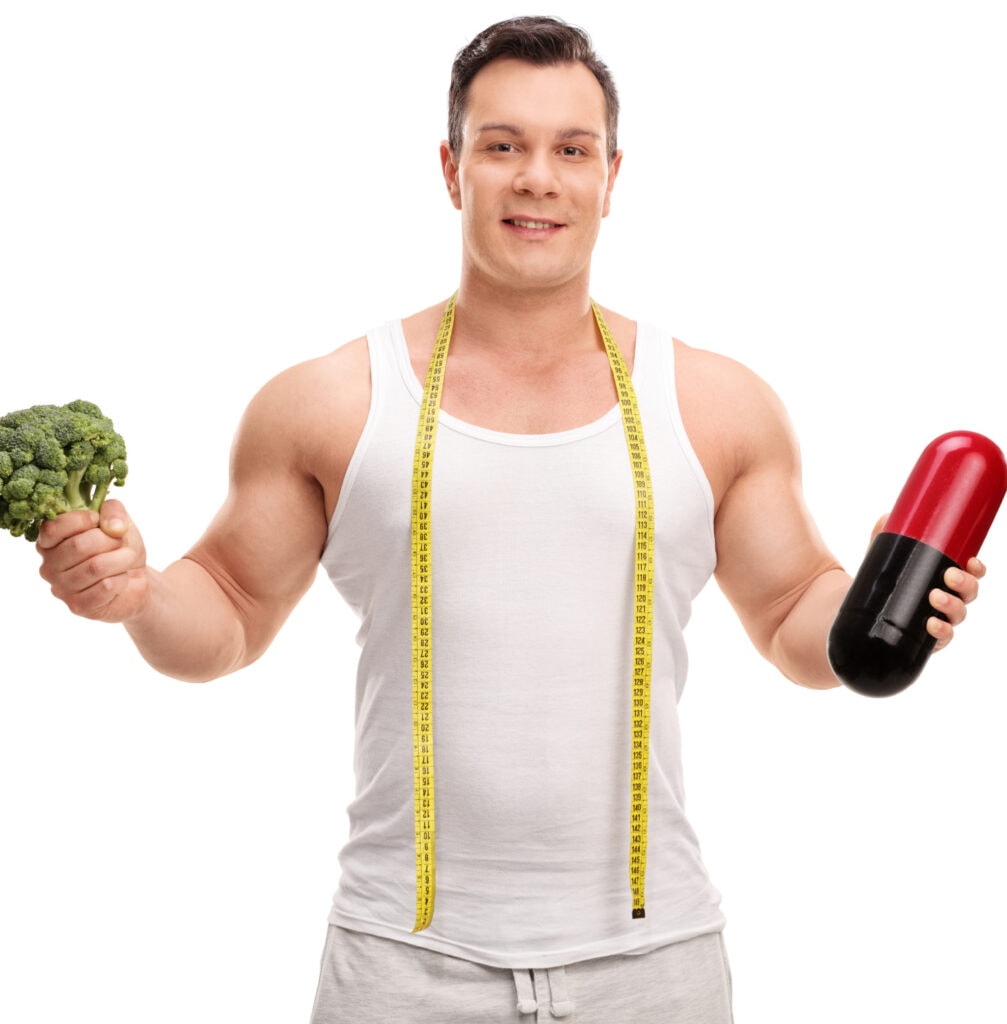 young healthy man holding broccoli in one hand and iron pill in other hand
