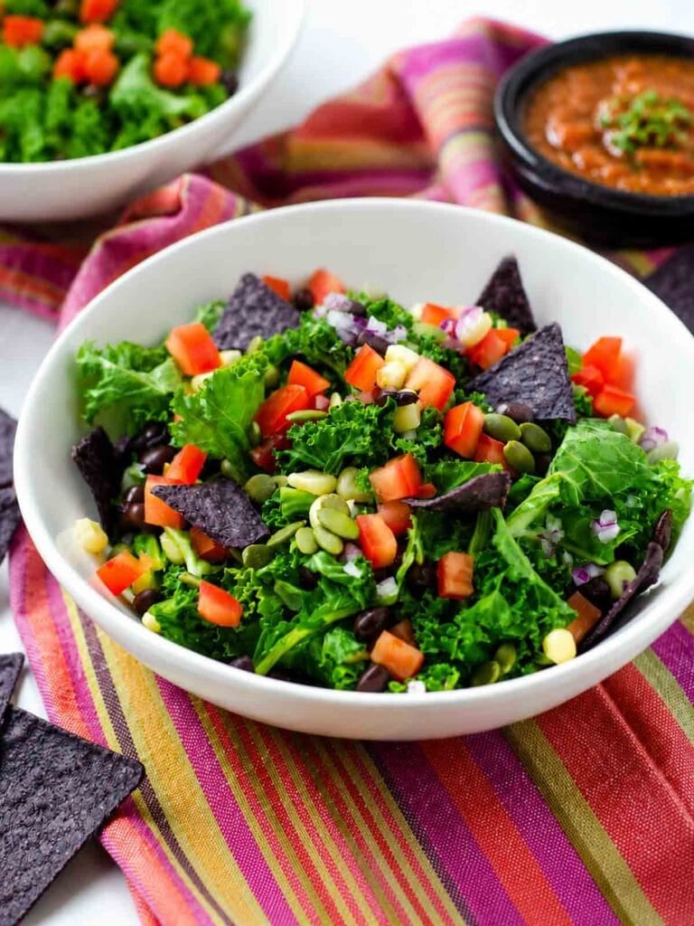 mexican cake salad with blue cornchips in a white bowl.