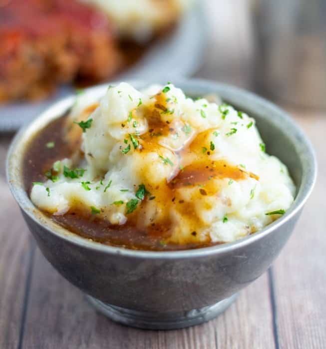 mashed potatoes covered with brown gravy in silver bowl on wooden table