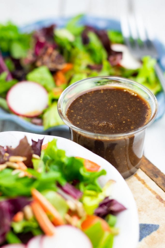 oil free salad dressing in clear glass cup surrounded by plates of salad