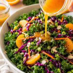 orange miso dressing being poured over a kale salad with purple cabbage and orance slices.
