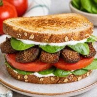 smoked tempeh bacon sandwich with tomato, lettuce, and tofu mayonnaise on a plate.