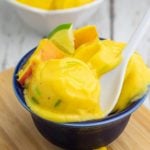 blue bowl filled with scoops of mango ice cream with white spoon dipped in