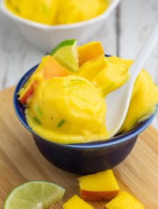blue bowl filled with scoops of mango ice cream with white spoon dipped in
