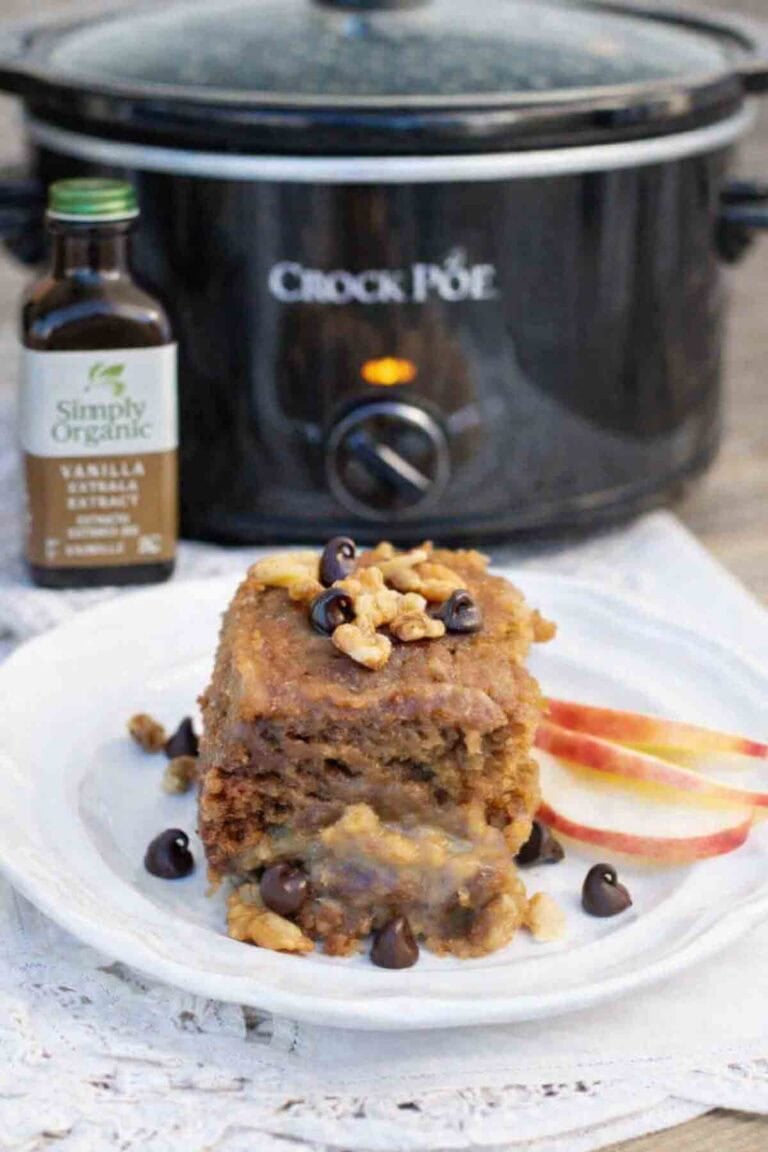 a slice of vanilla crock pot cake on a white plate with a crock pot in the background.
