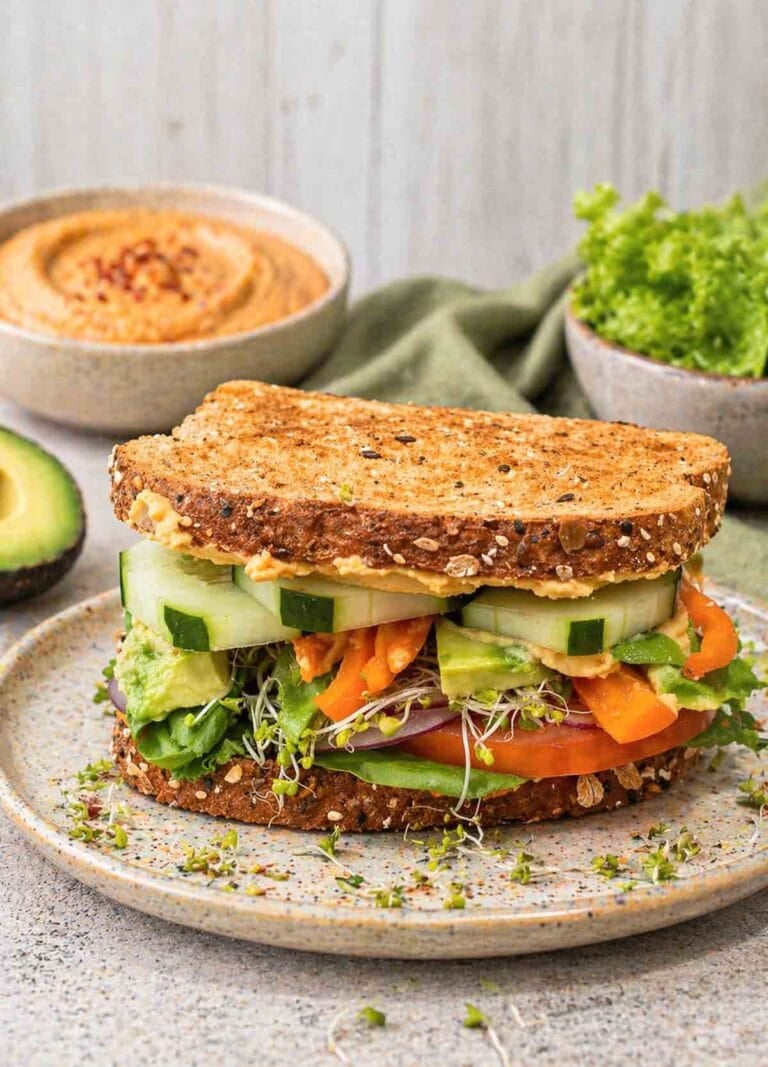 hummus sandwich piled high with tomato, lettuce, cucumbers, avocado, beansprouts.