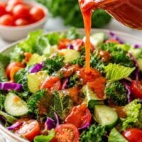tangy tomato salad dressing being poured from a jar onto a colorful salad.