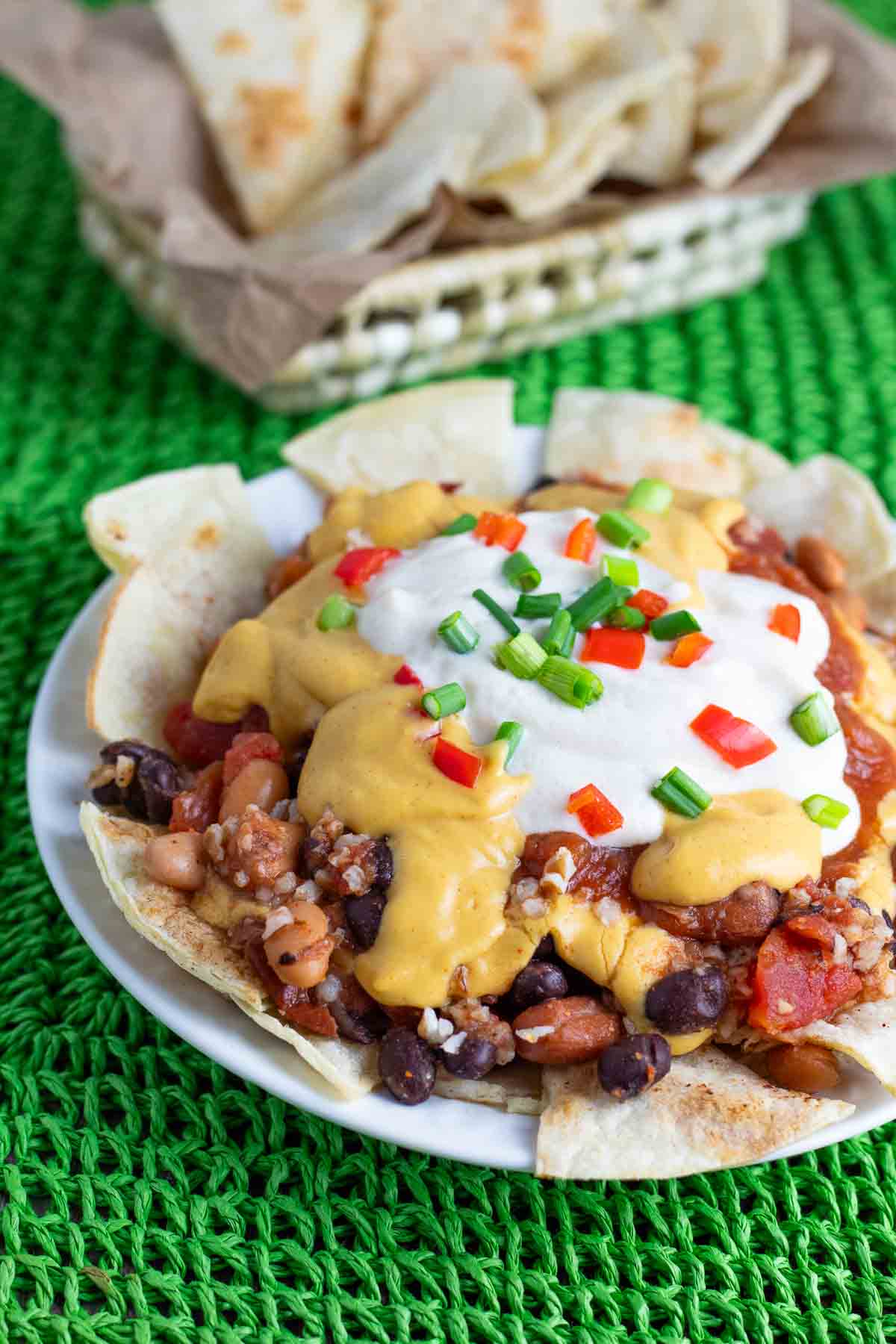 healthy vegan nacho supreme with tortilla chips on a platter topped with vegan cheese sauce and sour cream.