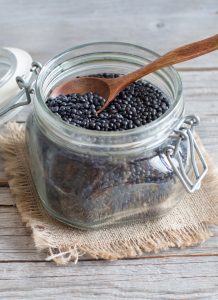 black lentils in clear jar with wooden spoon