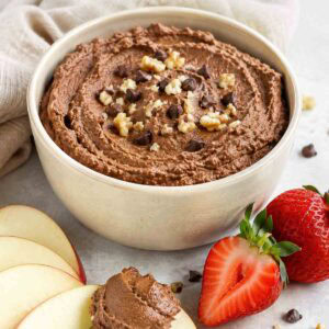 chocolate hummus in a bowl with apple slices and strawberries surrounding the bowl.