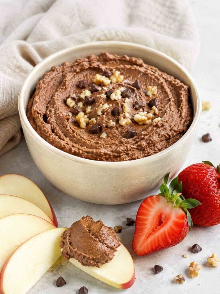 chocolate hummus in a bowl with apple slices and strawberries surrounding the bowl.