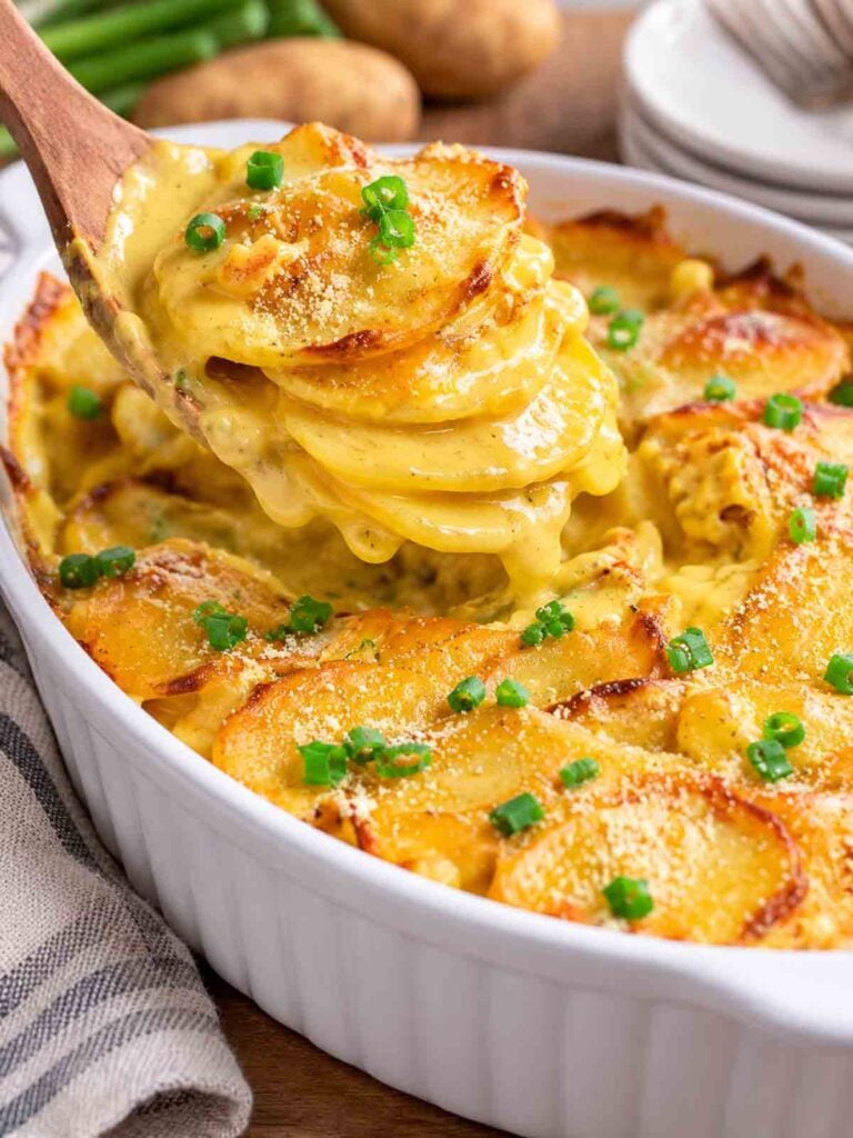 scalloped potatoes in an oval casserole dish being served in a wooden spoon.