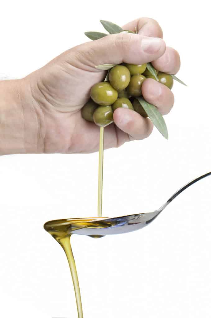 A hand squeezing olives and getting olive oil into a spoon.
