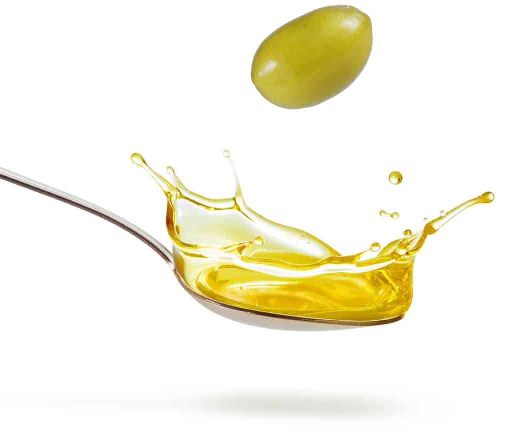 green olive falling into a spoon of oil