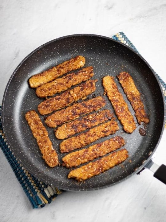 overhead photo of tempeh bacon in nonstick skillet on white background
