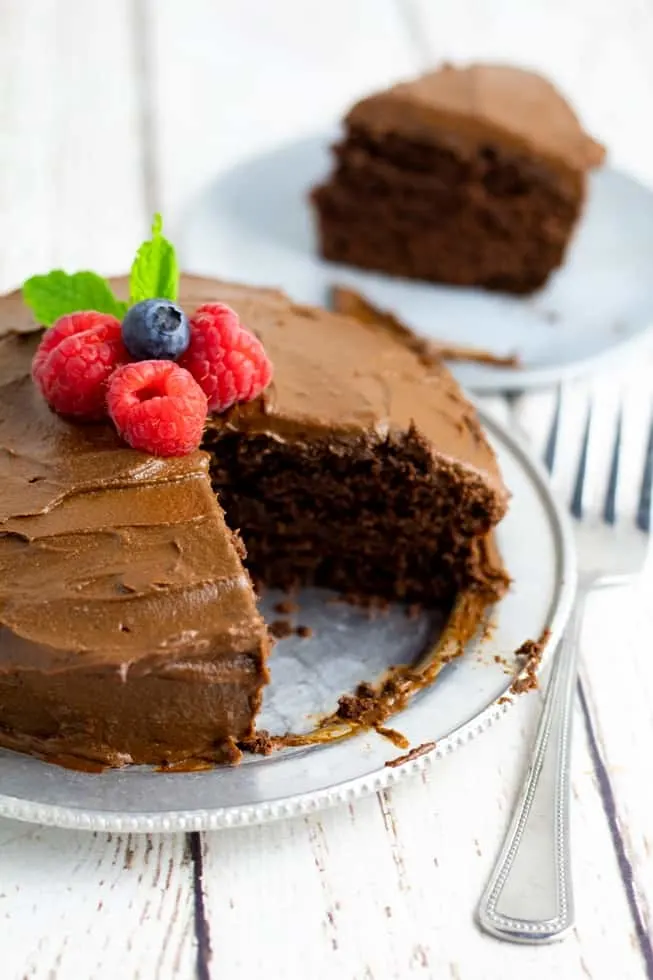 healthy chocolate cake with slice missing on silver plate topped with berries
