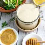 overhead shot of honey mustard in glass container with saucer of mustard and saucer of honey and salad