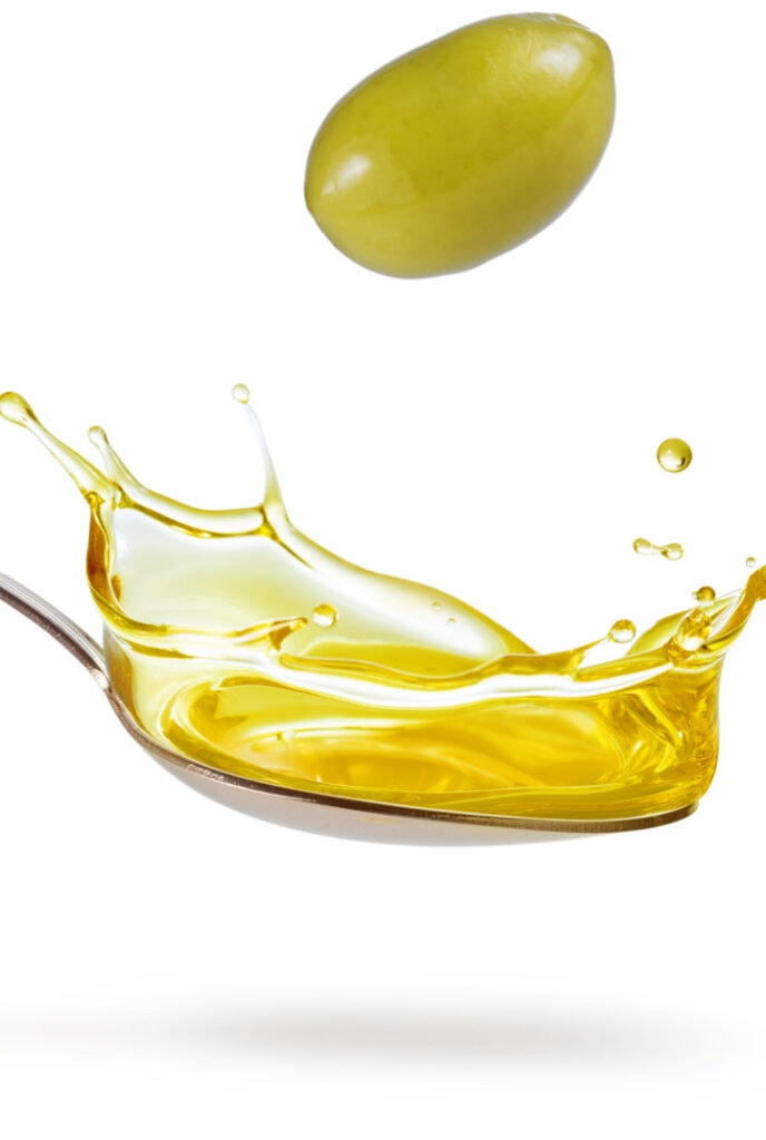 green olive falling on a splashing spoon of oil isolated on white