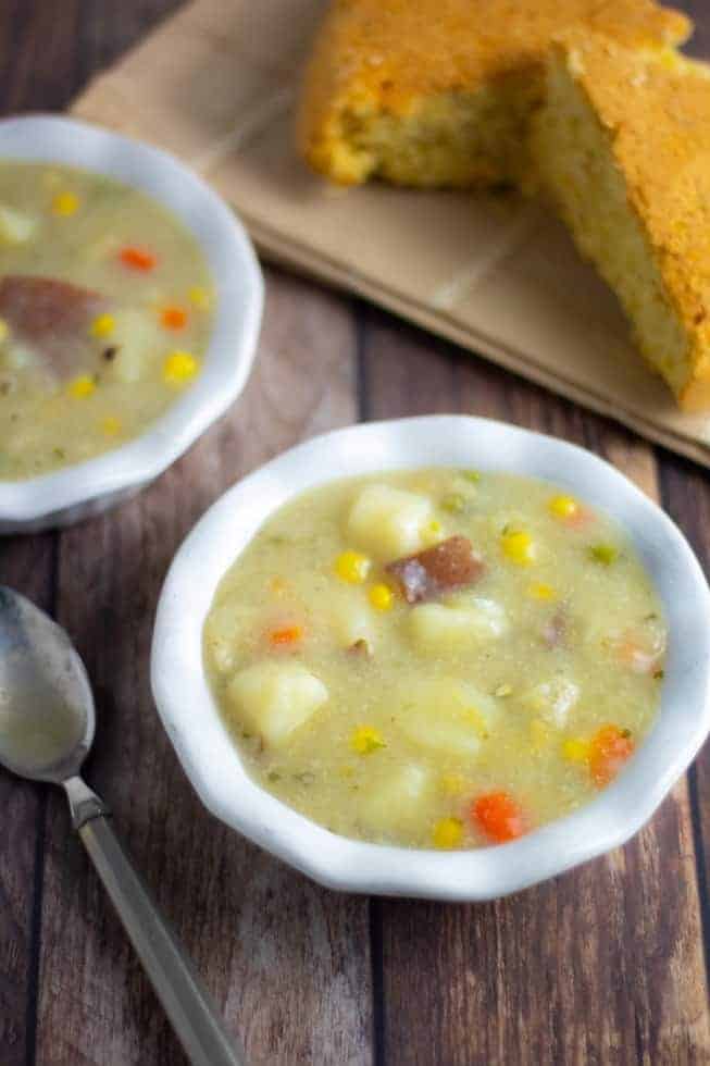 vegan potato soup in white bowls on wooden table with cornbread