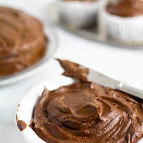 sugar free chocolate icing in white bowl with cake and cupcakes in background
