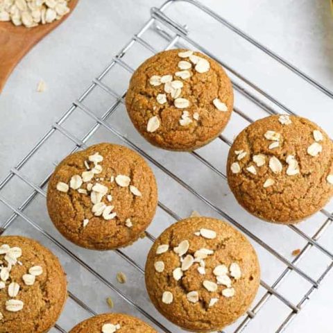 vegan muffins on cooling rack with oats sprinkled over the top on white background