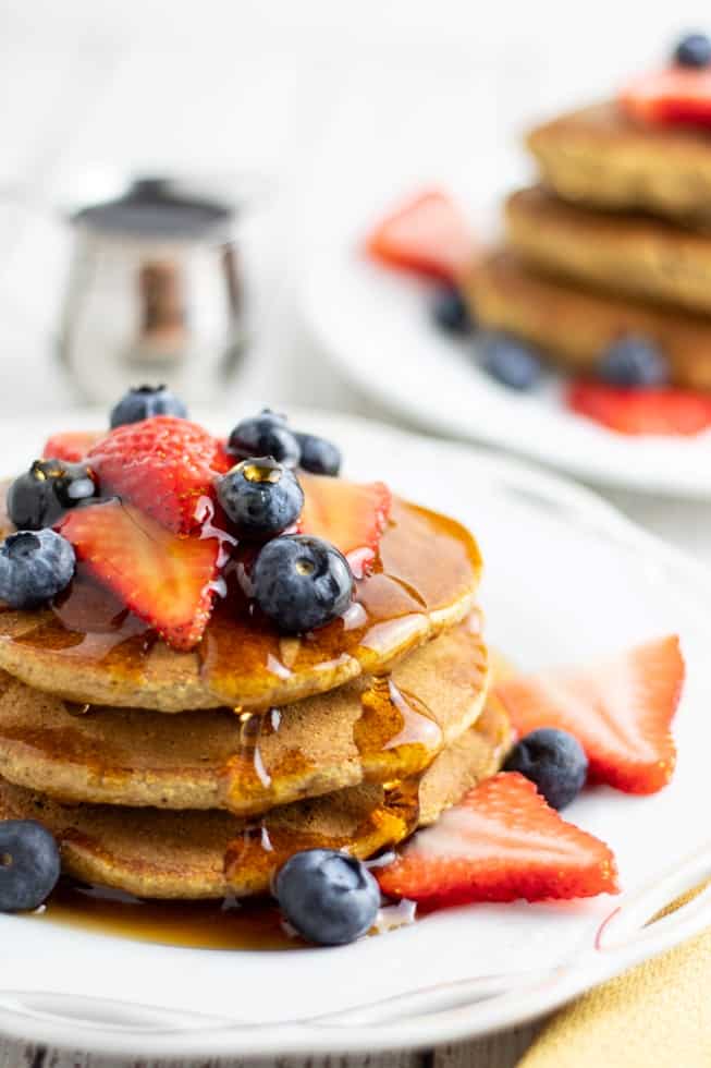 Banana oat flour pancakes topped with blueberries and strawberries on white plate